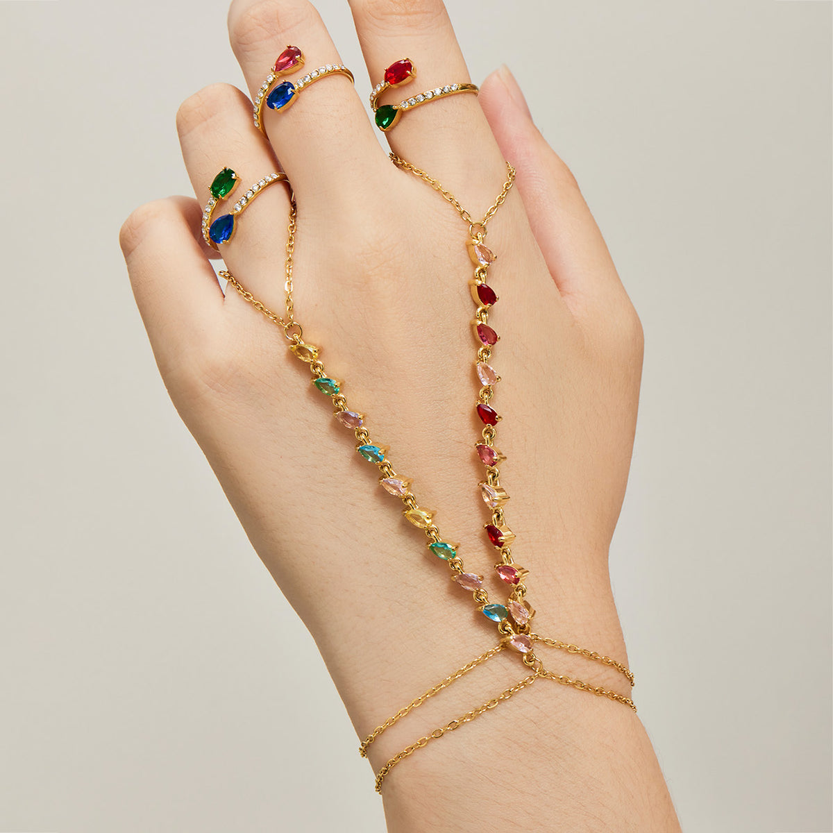 Red and multicolor cubic zirconia hand chain bracelets in gold tone worn across the back of the hand