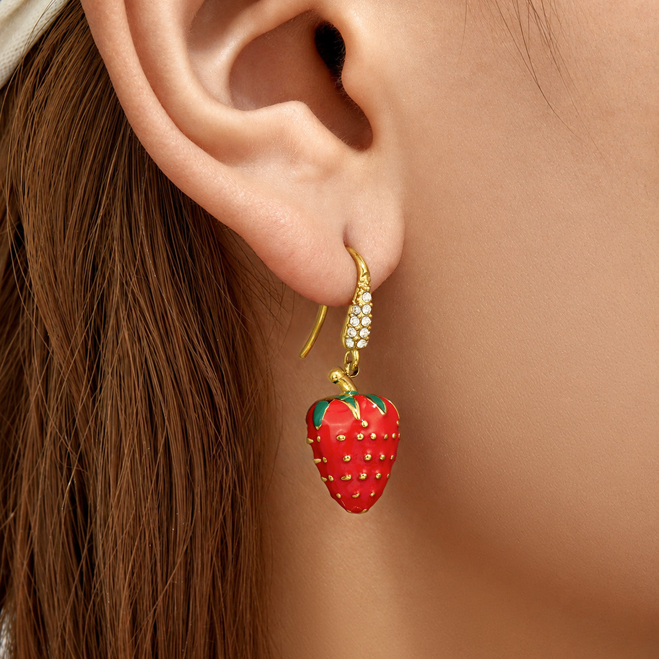 Side view of red strawberry drop earrings worn on the ear