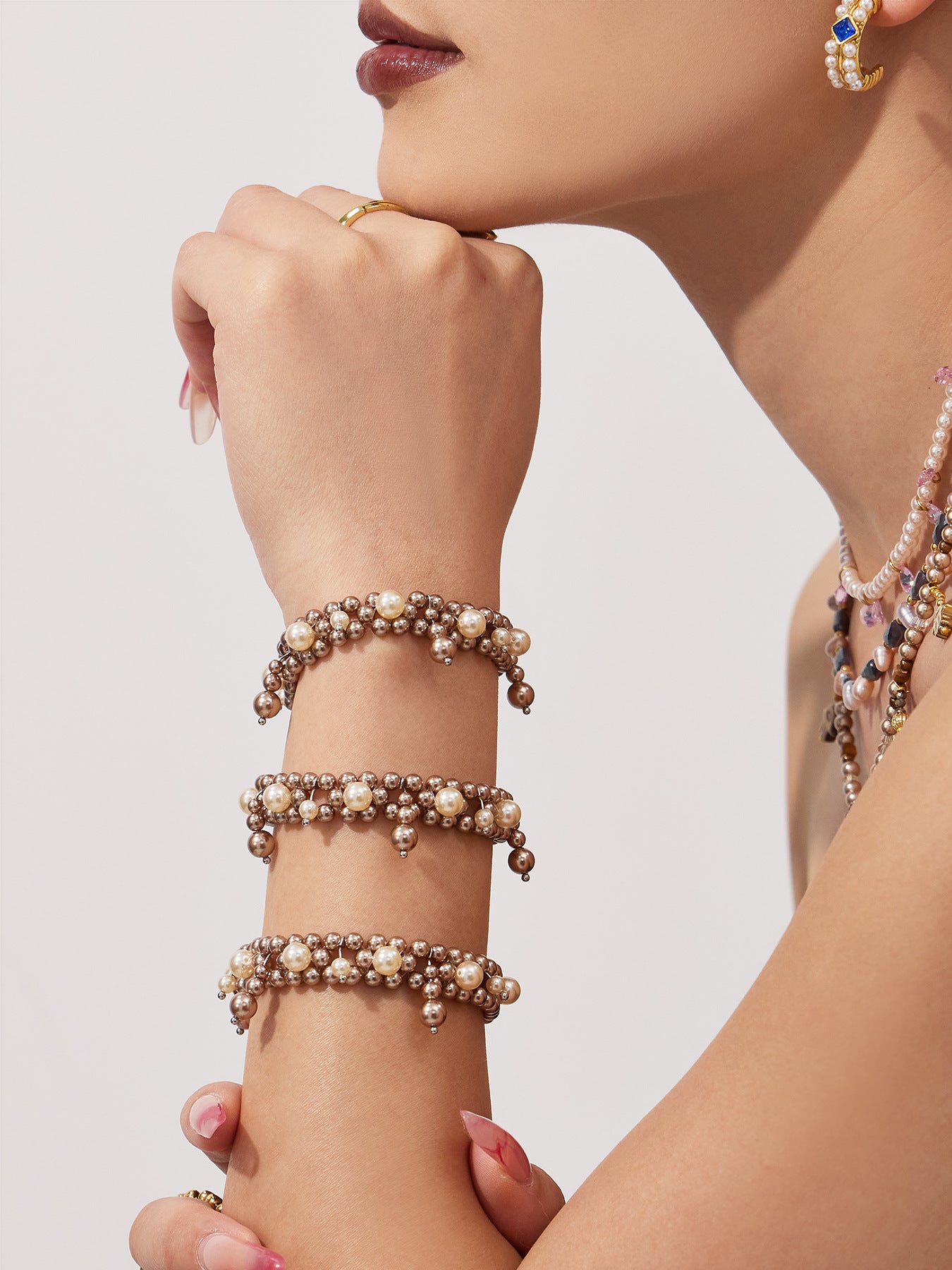 Model holding her hand near her face while wearing stacked shell pearl bracelets