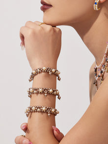 Model holding her hand near her face while wearing stacked shell pearl bracelets