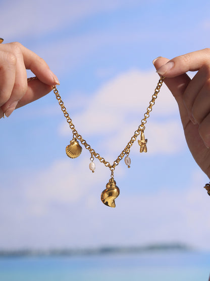 Hand holding gold shell pearl charm anklet against blue beach sky, adjustable stainless steel chain for vacation styling
