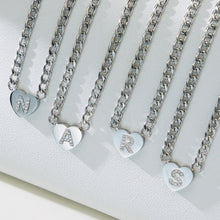 Silver-tone zircon initial heart necklaces displayed in multiple letter variants on a white jewelry stand