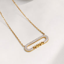 Single gold MAMA zircon bar necklace displayed on softly draped fabric