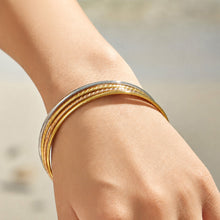 Model wearing slim gold-tone stackable bangles on the wrist