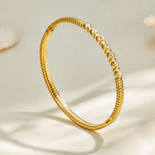 Slim gold zircon bangle displayed upright with decorative stone details