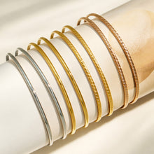 Slim stackable bangles in mixed steel, gold and rose gold finishes displayed on a cushion