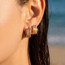 Model wearing compact gold zircon huggie earrings against a beach background