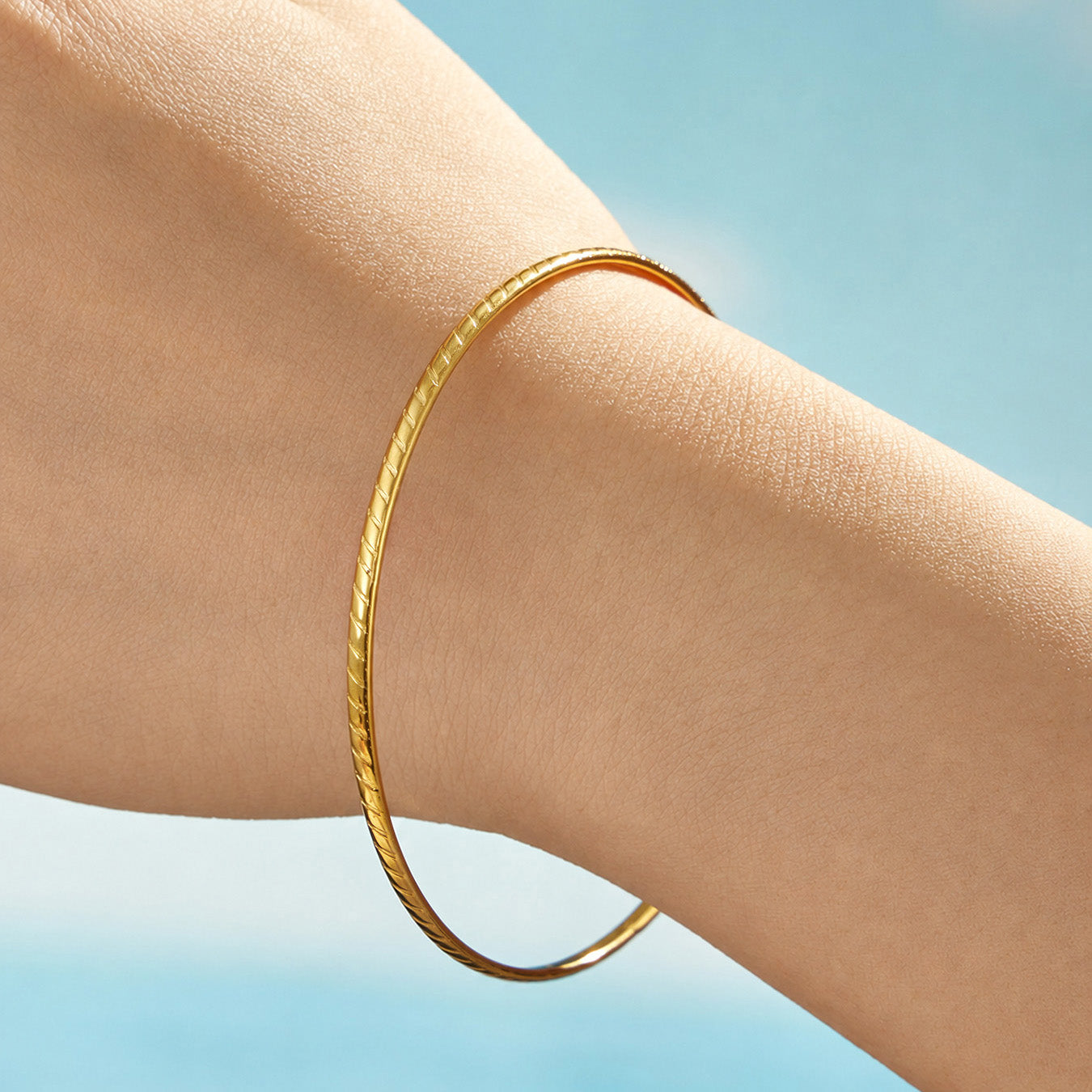 Side view of a model wearing a smooth slim gold-tone stainless steel bangle
