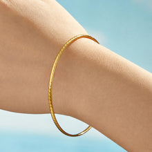 Side view of a model wearing a smooth slim gold-tone stainless steel bangle