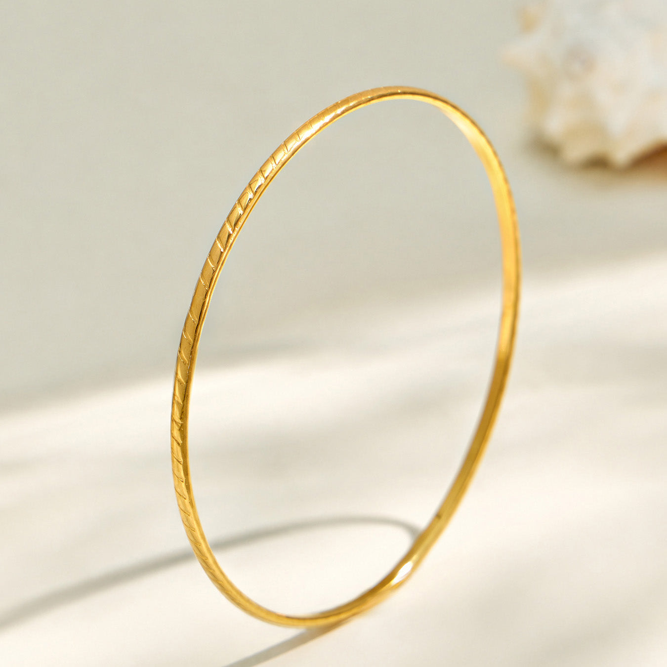 Smooth gold-tone slim stainless steel stackable bangle on a light background
