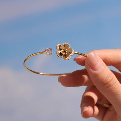 18K gold plated sparkling zircon flower thin open bangle, held in hand against sky background