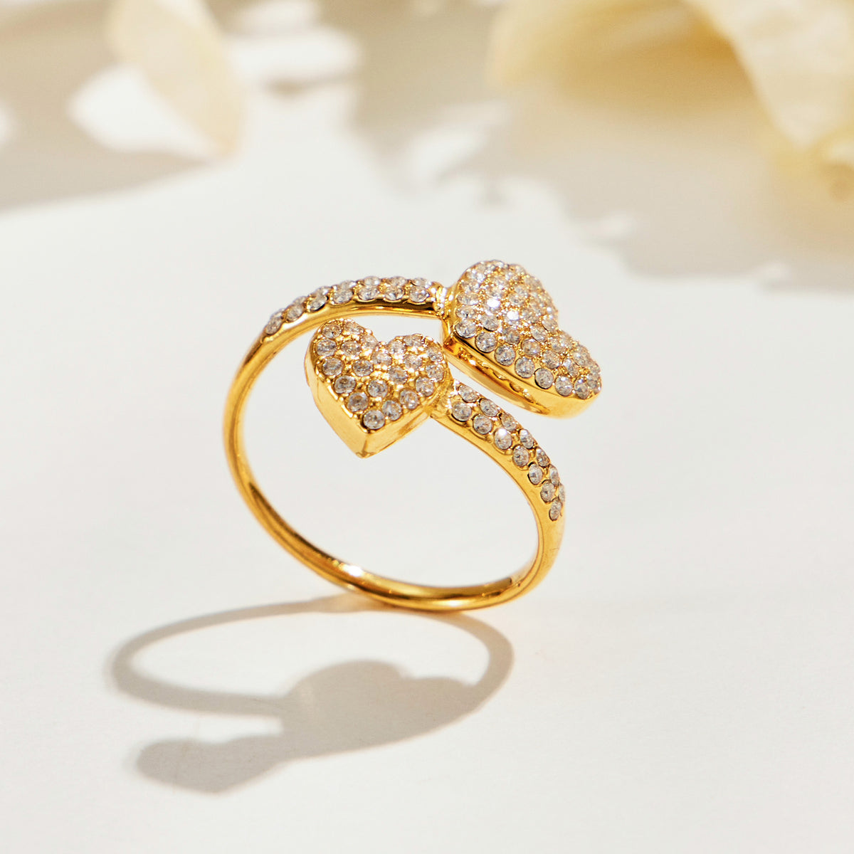 A457 gold-tone pave-heart open ring standing on a cream surface, showing two stone-covered hearts