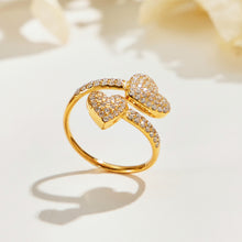 A457 gold-tone pave-heart open ring standing on a cream surface, showing two stone-covered hearts