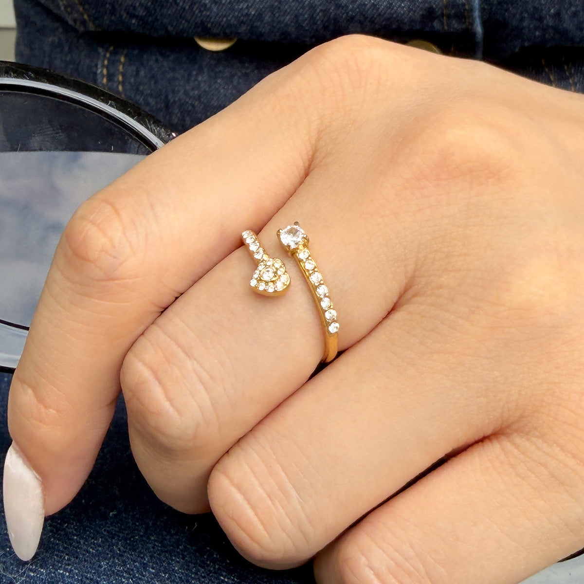 A635 gold-tone heart open ring worn on a finger, showing a small clear-stone heart and stone-set band
