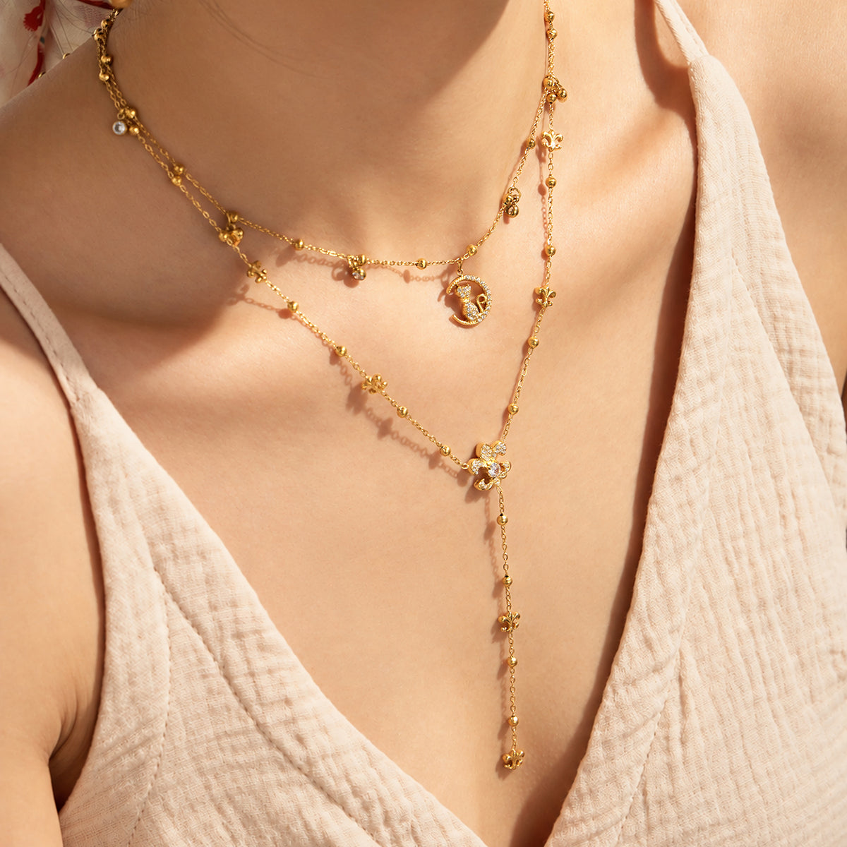 Close-up of layered gold-tone stainless steel cat moon and Y lariat necklaces, with a hand resting near the neck