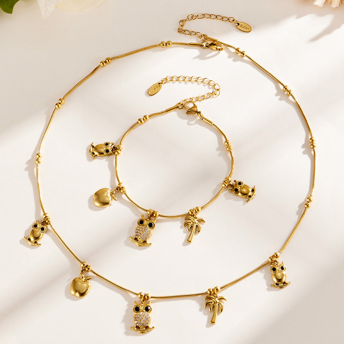 Stainless steel charm necklace and bracelet flat lay with animal, apple and tropical charms