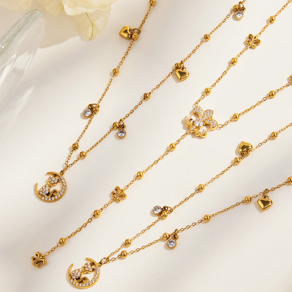 Gold-tone stainless steel cat moon charm necklaces and an ornamental Y lariat arranged diagonally on a cream surface