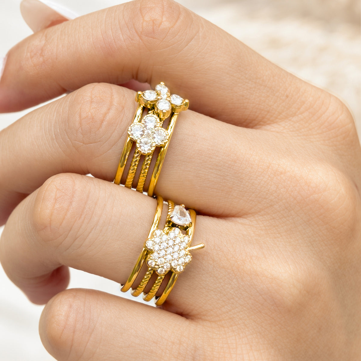 Two gold-tone stainless steel floral cluster rings worn on fingers, showing clear stones and layered bands