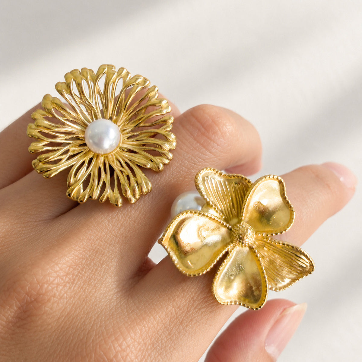 Close-up of gold-tone stainless steel openwork and sculpted flower rings with white faux pearls worn on a hand