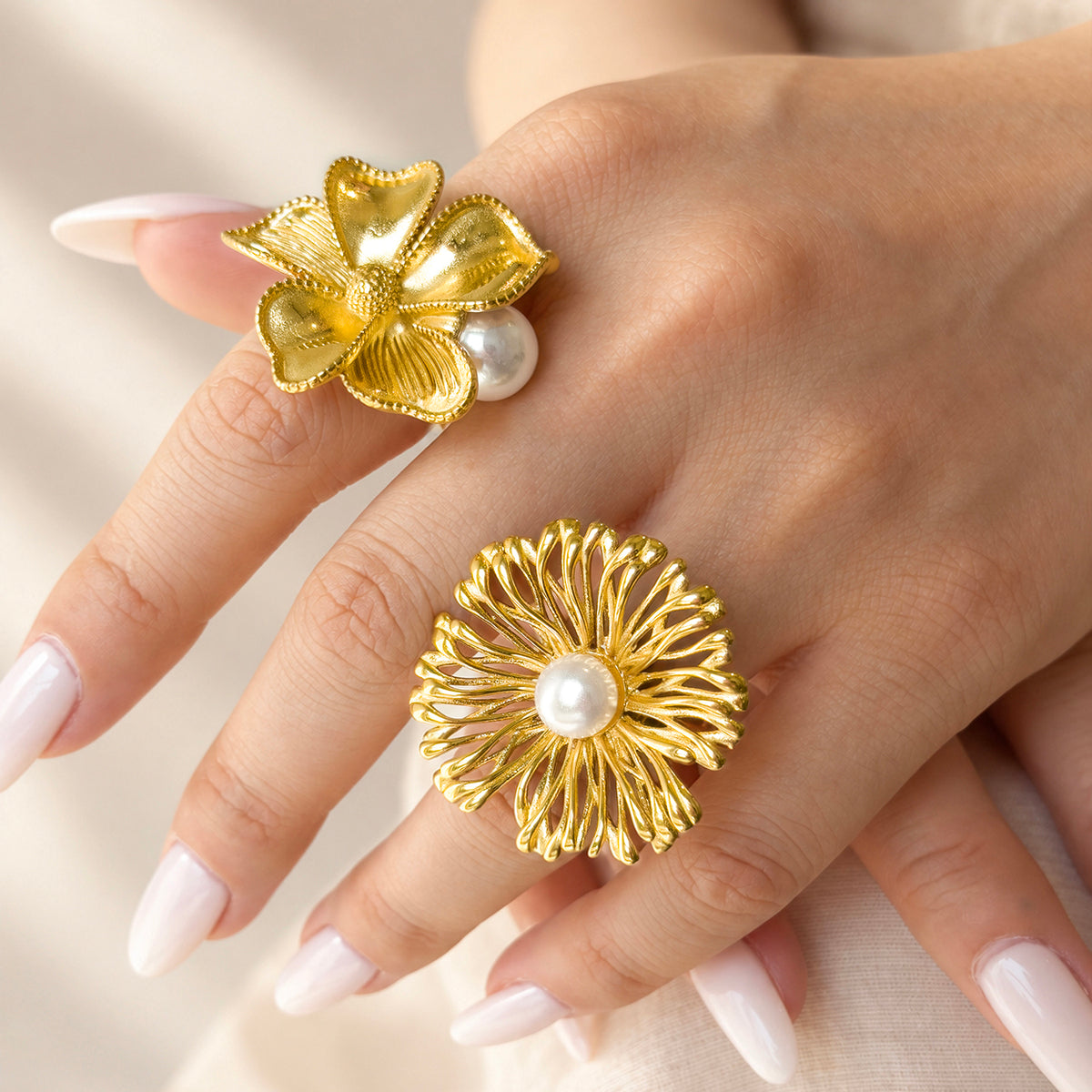 Gold-tone stainless steel flower statement rings with faux pearl accents styled on a hand with white nails