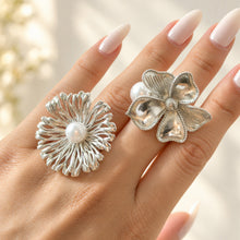 Silver-tone stainless steel openwork and sculpted flower rings with white faux pearl accents worn on a hand