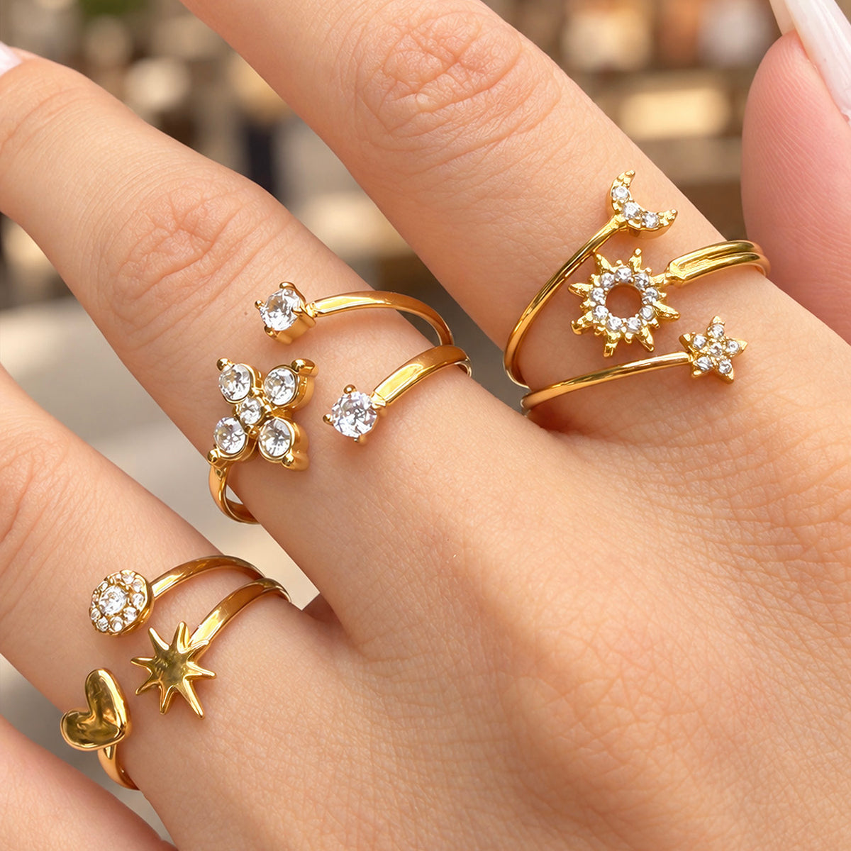 Close-up of gold-tone celestial, flower and heart-star open rings worn together