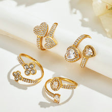 Four gold-tone stainless steel flower, heart and two-stone open rings displayed on a cream surface
