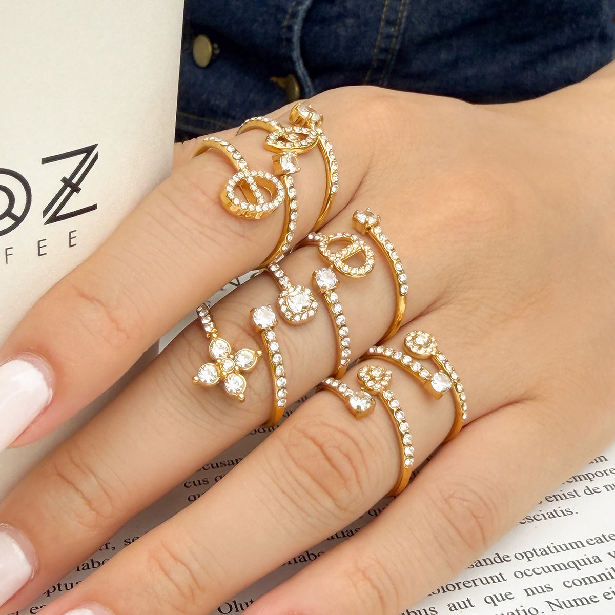 Gold-tone stainless steel open rings worn on a hand beside denim and a printed page
