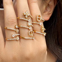 Gold-tone open rings with floral and geometric clear-stone details worn on a hand near the face