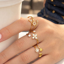 Side view of gold-tone celestial, flower and heart-star rings worn on a hand beside a cup
