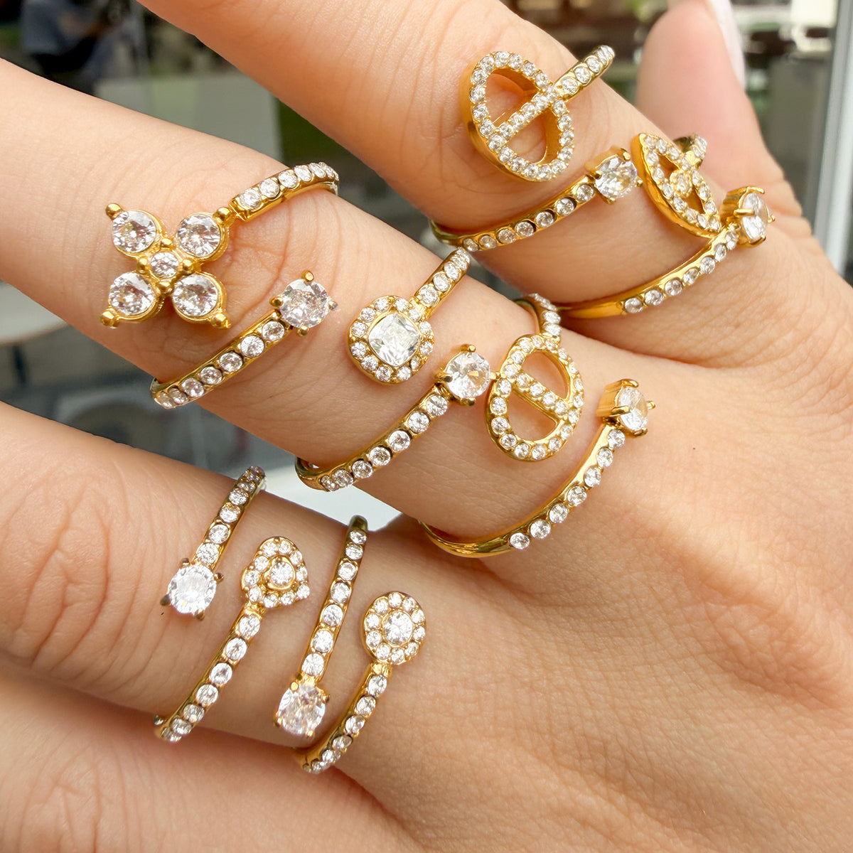 Multiple gold-tone stainless steel open rings styled across overlapping hands, showing different decorative motifs
