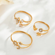 Three gold-tone stainless steel celestial, flower and heart-star open rings arranged on a cream surface