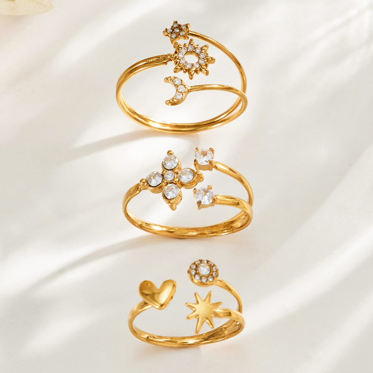Three gold-tone open rings displayed upright, showing sun-moon-star, flower and heart-star designs