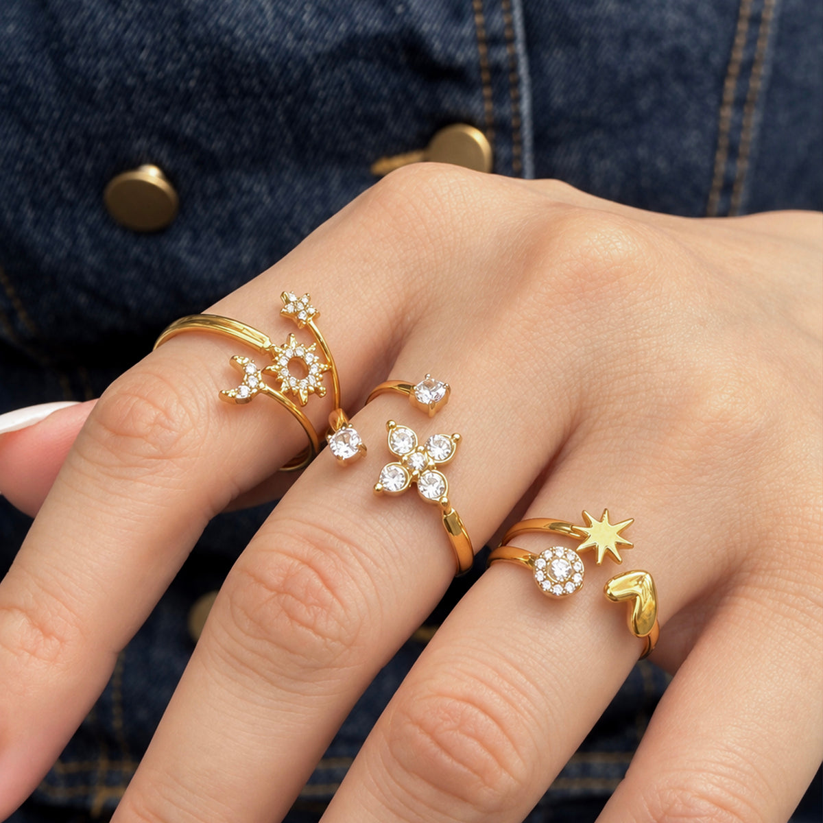 Three gold-tone stainless steel open rings worn across fingers against denim