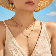 Model wearing layered gold-tone stainless steel cat moon and Y lariat necklaces with a straw hat and cream V-neck top