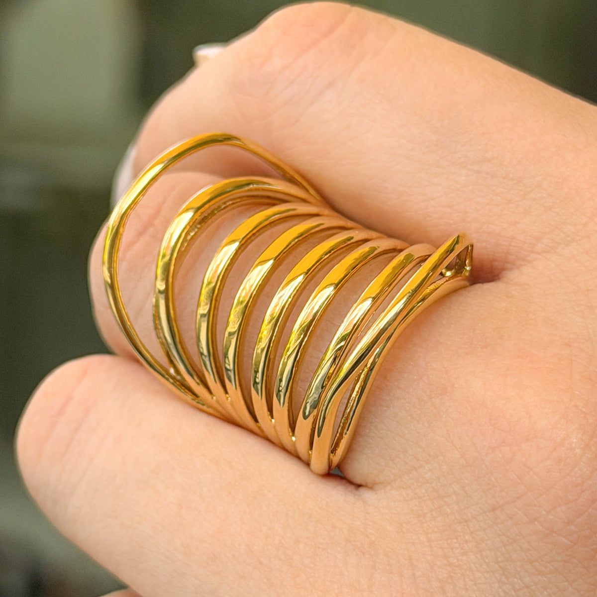 Close-up side view of a gold-tone stainless steel statement ring with sweeping curved bands and open spaces