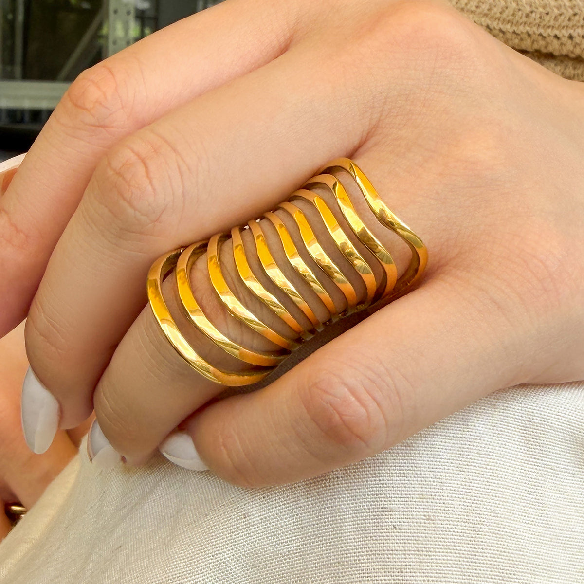 Gold-tone stainless steel multi-band statement ring worn on a hand resting against white knit fabric
