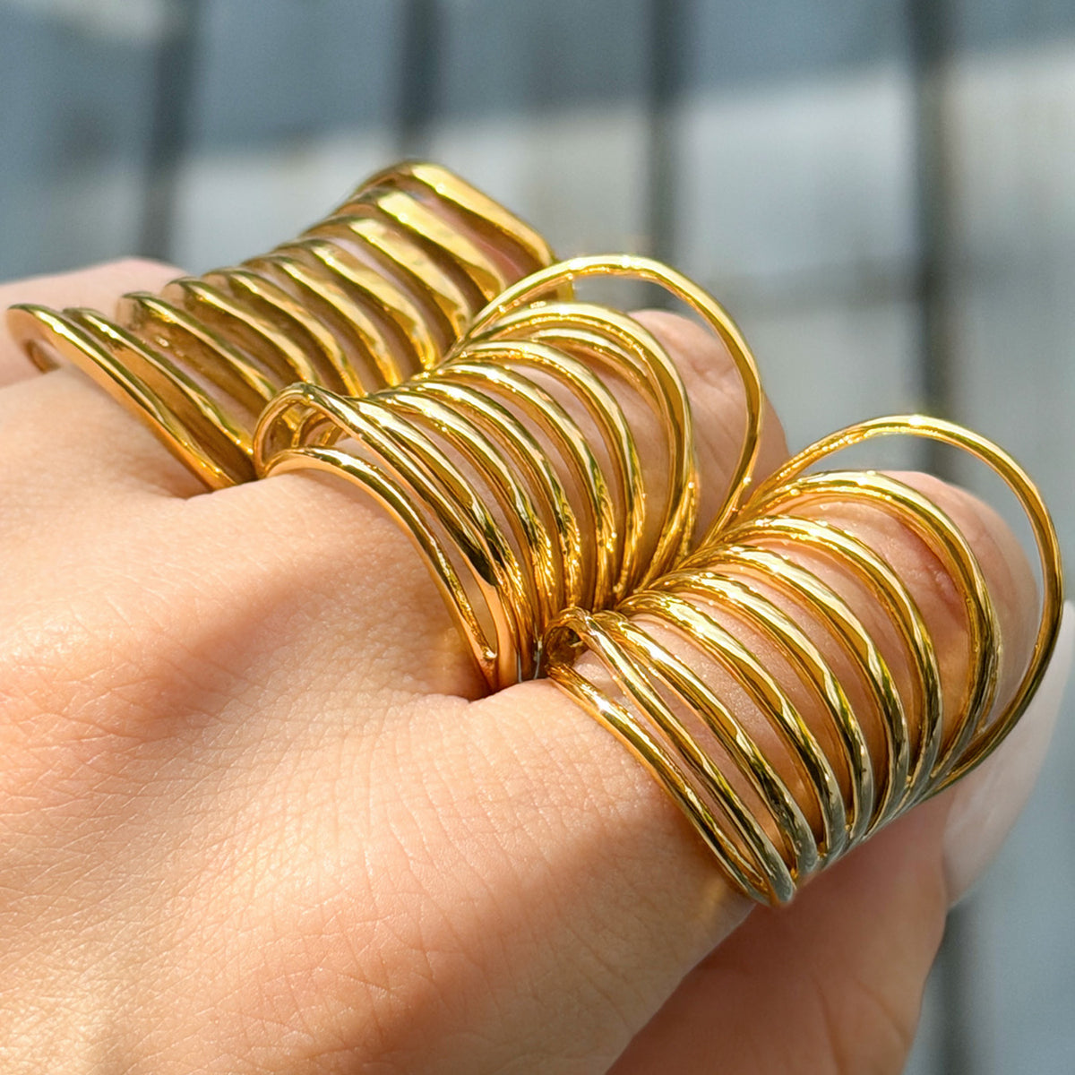Side view of three gold-tone stainless steel rings worn on a hand, highlighting their raised curved bands