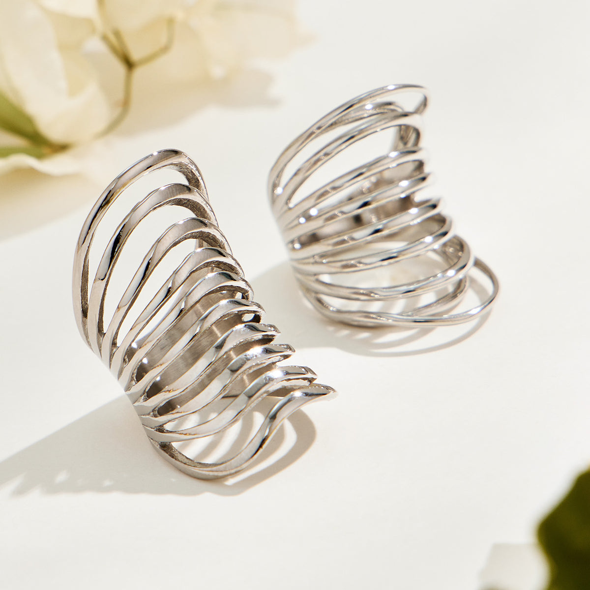Two silver-tone stainless steel openwork rings displayed in natural light, showing their sweeping curved bands