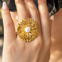 Gold-tone stainless steel openwork flower statement ring with a white faux pearl center worn on a finger