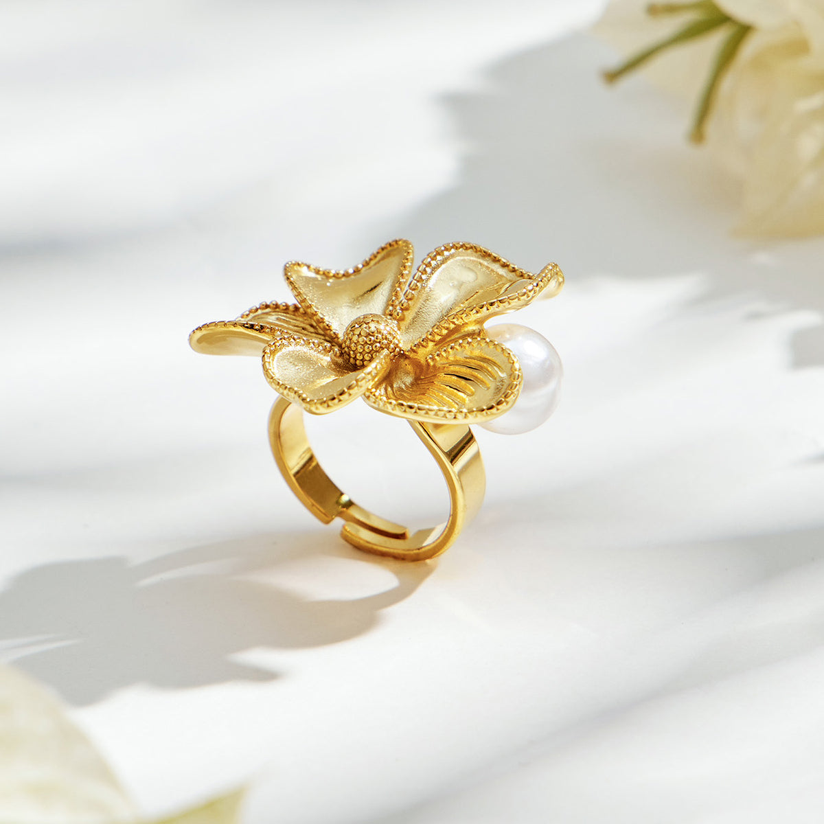 Gold-tone stainless steel sculpted flower ring with textured petals, a white faux pearl accent and an open band