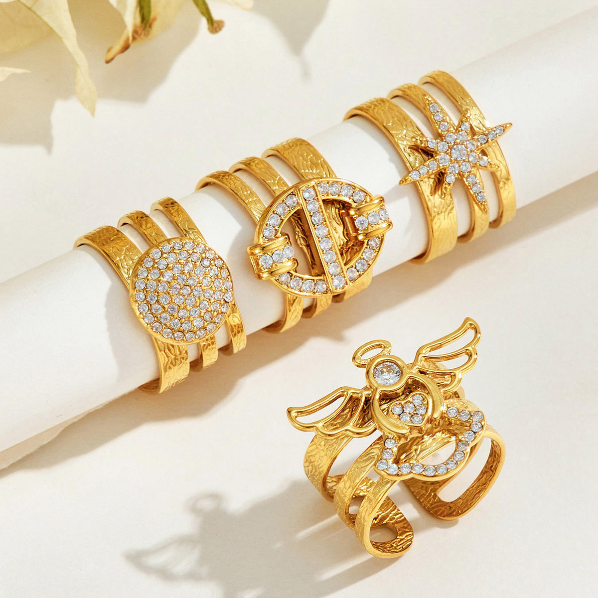 Gold-tone stainless steel rings displayed on a cream jewelry roll with an angel ring placed in front