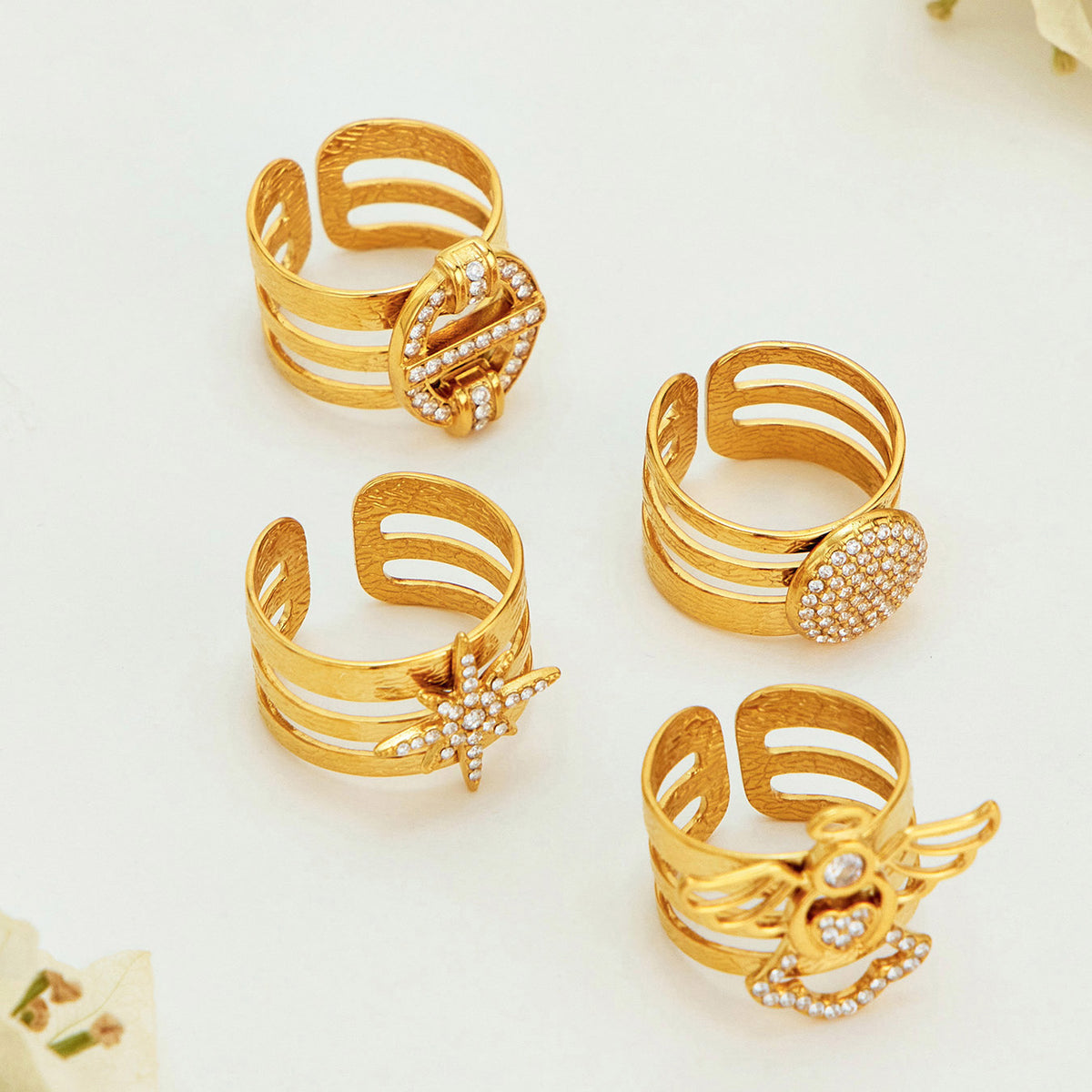 Rear views of four gold-tone stainless steel rings showing their open bands, layered construction and textured metal surfaces