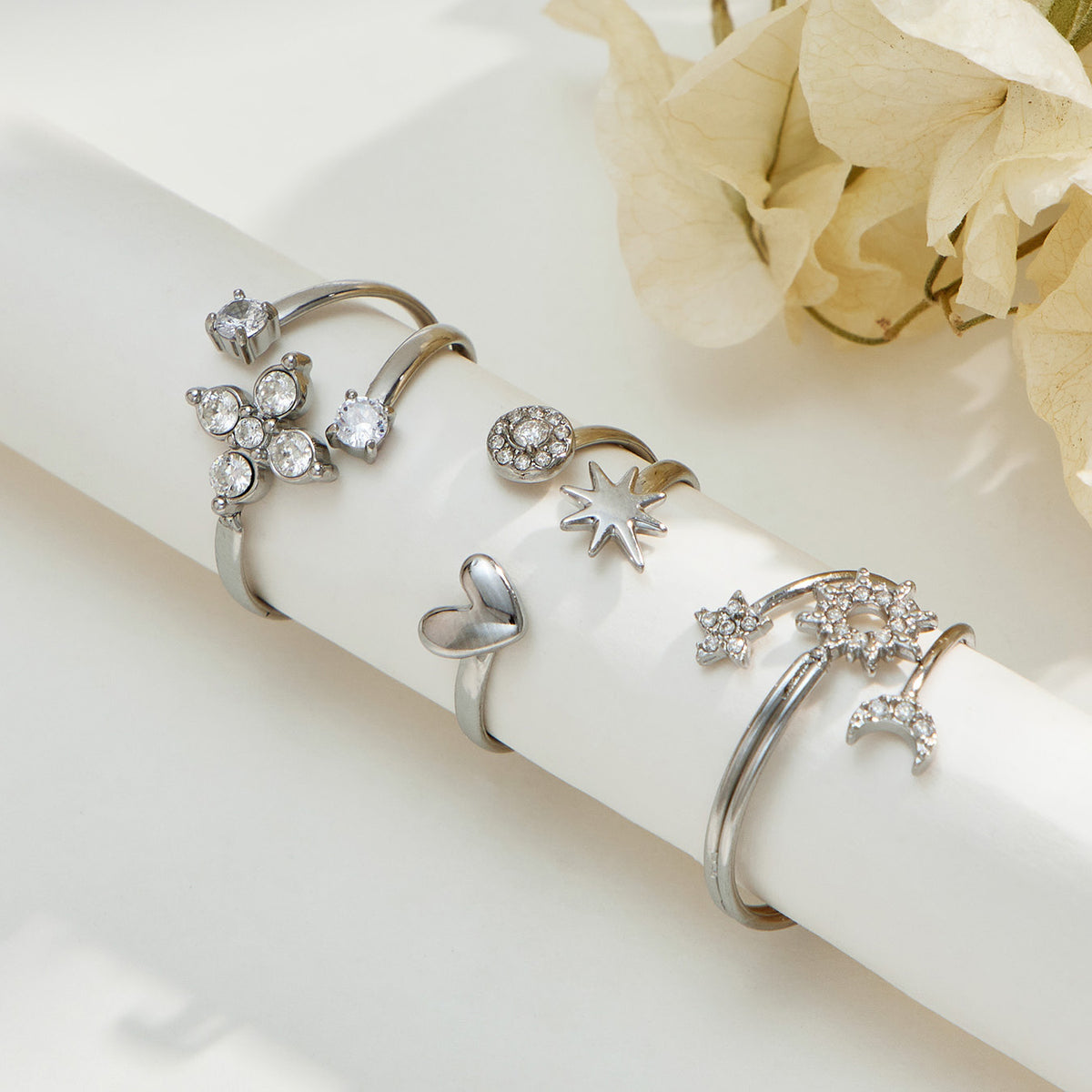 Steel-tone celestial, flower and heart-star rings displayed on a white cylindrical stand