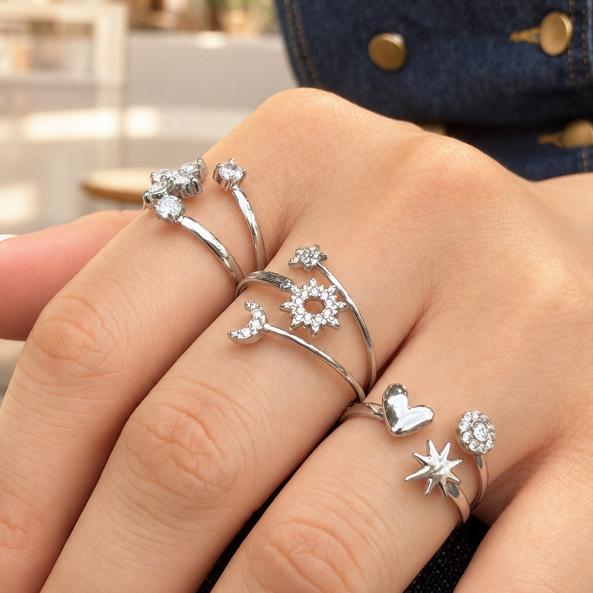 Three steel-tone stainless steel open rings with celestial, flower and heart-star designs worn on a hand