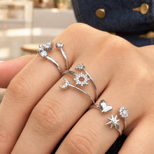Three steel-tone stainless steel open rings with celestial, flower and heart-star designs worn on a hand