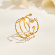 A403 gold-tone heart and bead ring standing on a cream surface, showing three slim textured bands