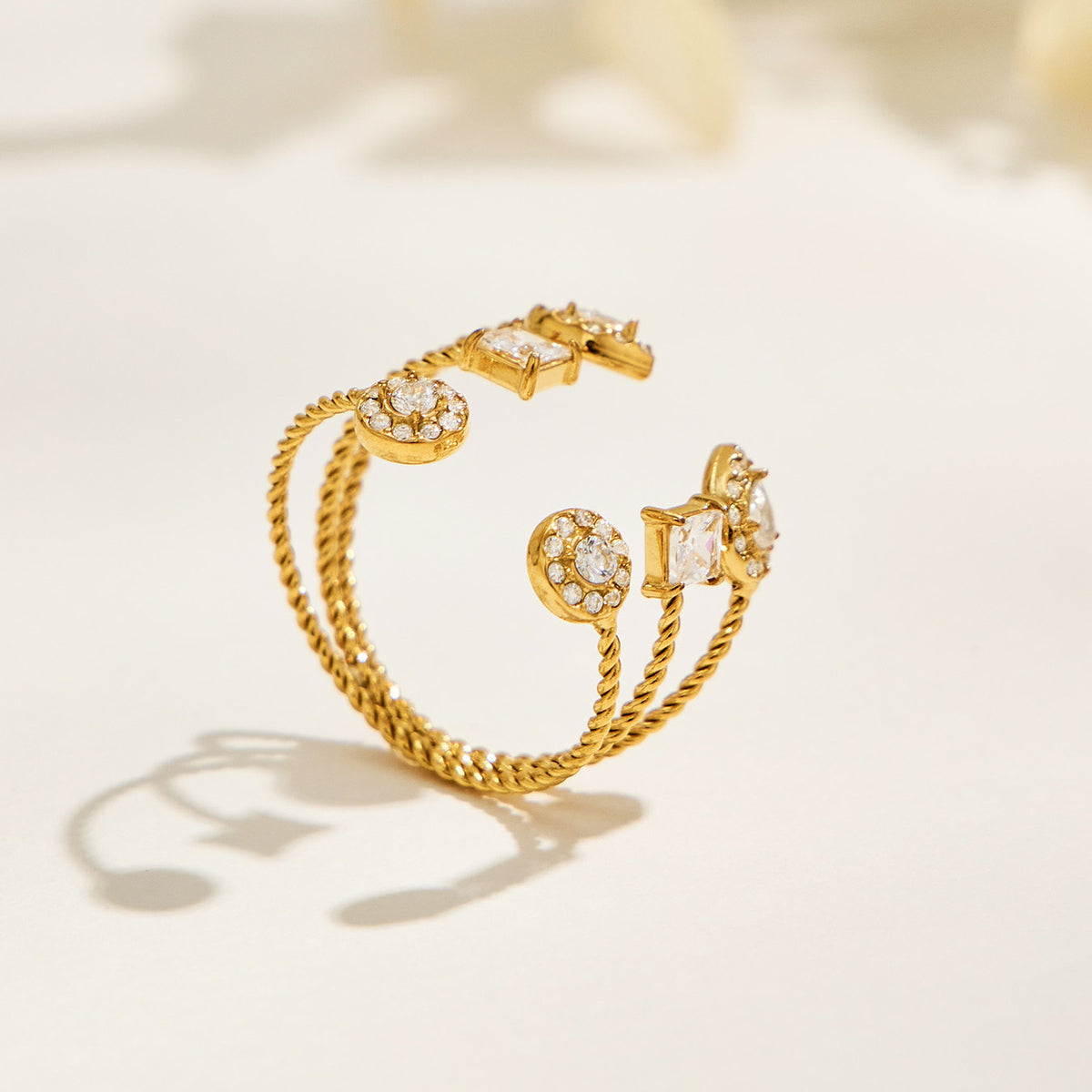 A406 gold-tone geometric open ring standing on a cream surface, showing circular and square decorative details