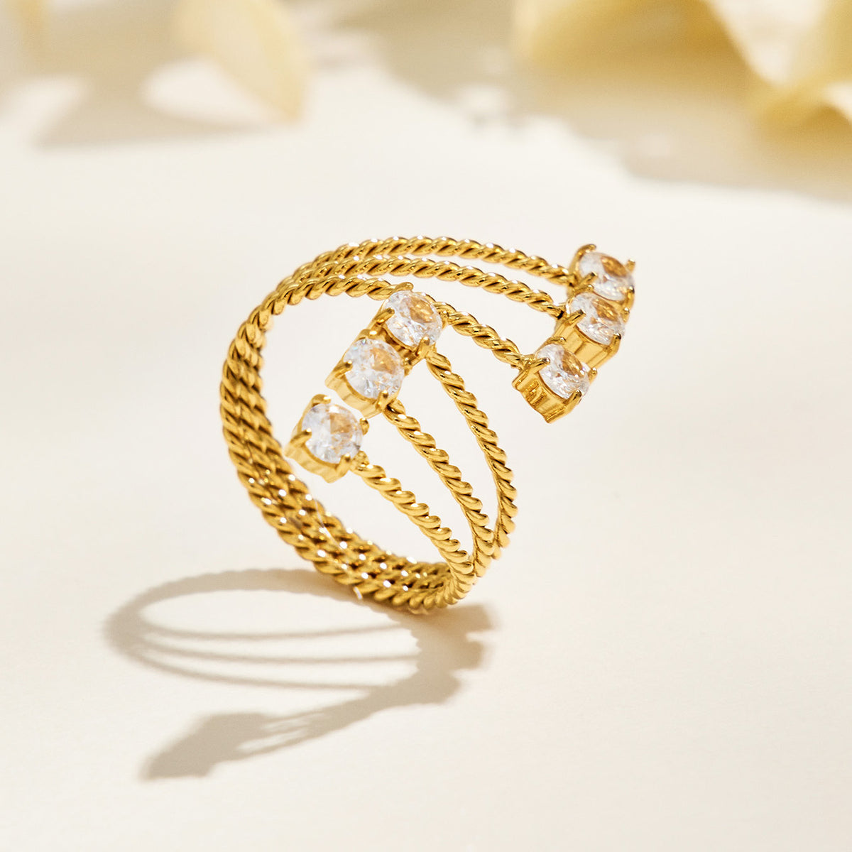 A420 gold-tone triple-band open ring standing on a cream surface, showing clear stone tips and textured bands