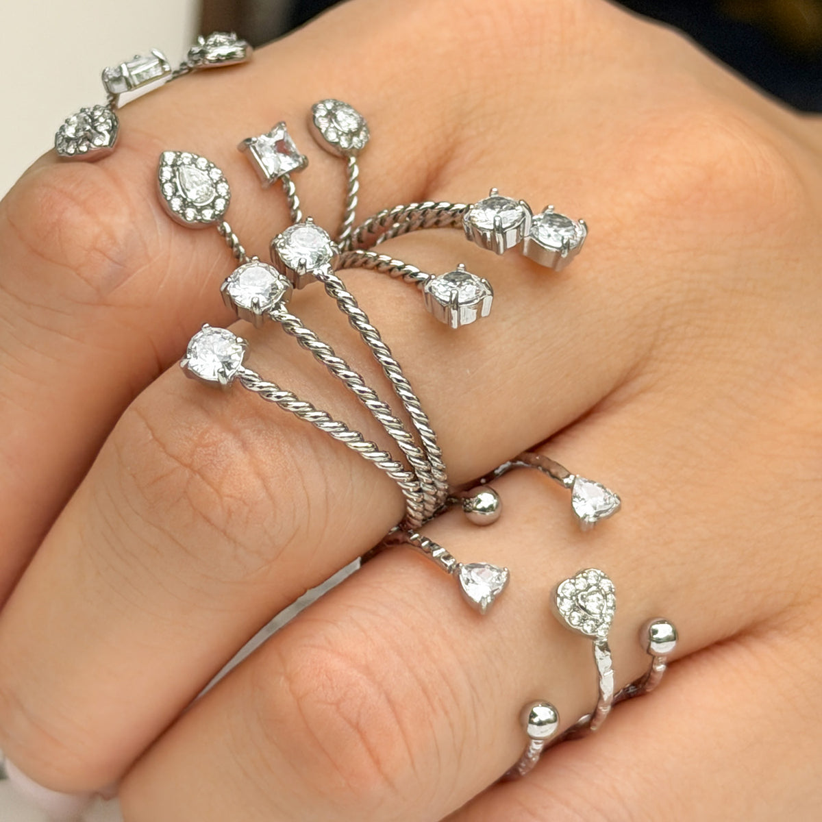 Three steel-tone stainless steel open rings worn together, showing heart, geometric and stone-tip designs